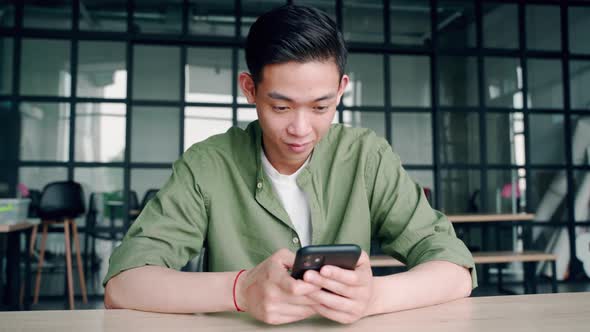 Young Happy Asian Chinese Student Sitting at Office Using Mobile Cell Phone