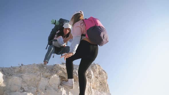 Girl Helps Her Friend Climb Up the Last Section of Mountain. Tourists with Backpacks Help Each Other