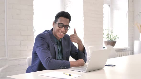 Thumbs Up By Businessman at Work Looking at Camera