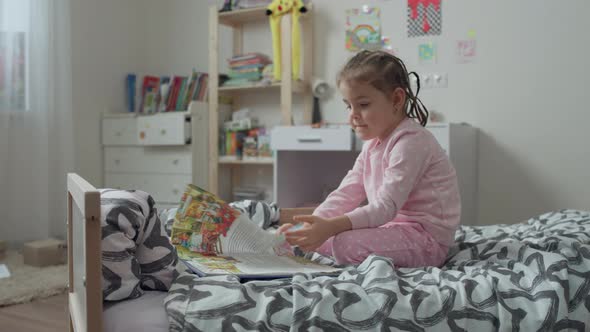 Caucasian Girl Reading a Book on the Bed in the Nursery