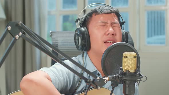 Boy In Headphones Playing The Guitar And Singing Into Microphone While Recording Podcast In Studio