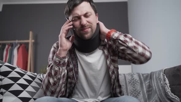 Disabled Man with Neck Brace Talking on Phone with Doctor Experiencing Pain While Sitting on Couch