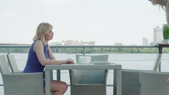 Elegant Adult Woman Greeting Friend in Outdoor Restaurant. Side View of Positive Adult Caucasian