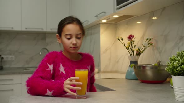 Shy Preteen Girl in Pink Sweater Taking Glass of Orange Juice at Home