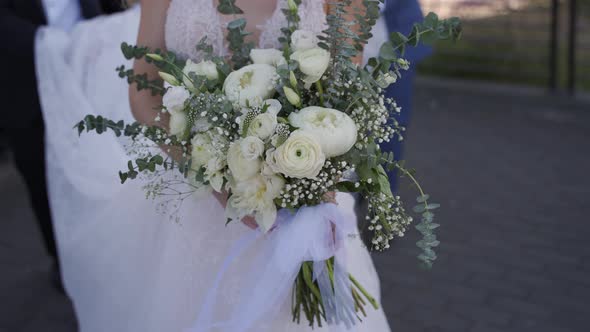 Handheld of young bride in a white wedding dress with a long tail and a bouquet of flowers in her ha