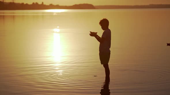 Boy with a Paper Ship is standing in the river. Origami Paper Boat in kid's hands. 