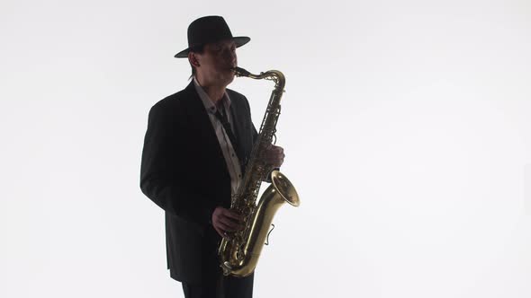 Male saxophonist in a suit and hat plays a gold saxophone. Skill of playing the saxophone.