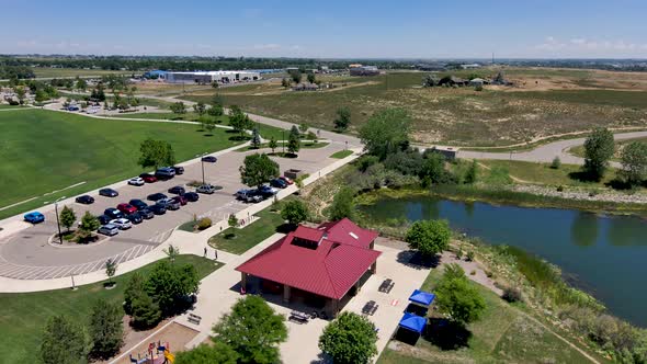 A park gazebo next to a lake and a full parking lot drone zoom.