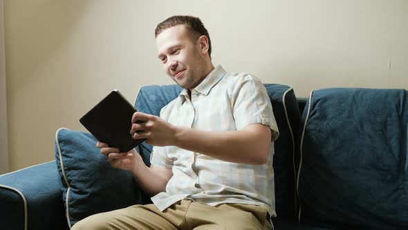 A Cheerful Young Guy Plays a Racing Simulator on a Tablet