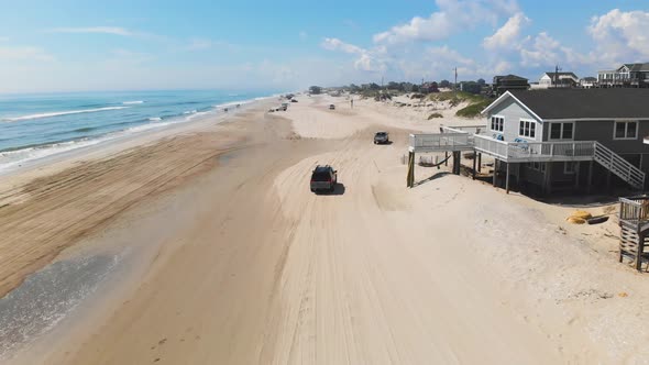 Drone following black suv and silver truck on Outer Banks Corolla 4x4 beach, houses can be seen inla