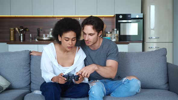 Diverse Boyfriend and Girlfriend Sitting Together on the Couch in Living Room and Clicking on