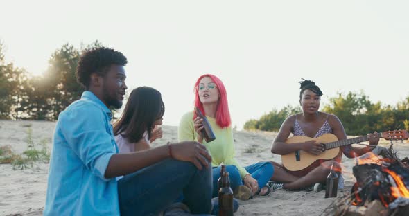 A Group of Students is Spending Time Together Sitting on Beach Near Lake They are Lighting Bonfire