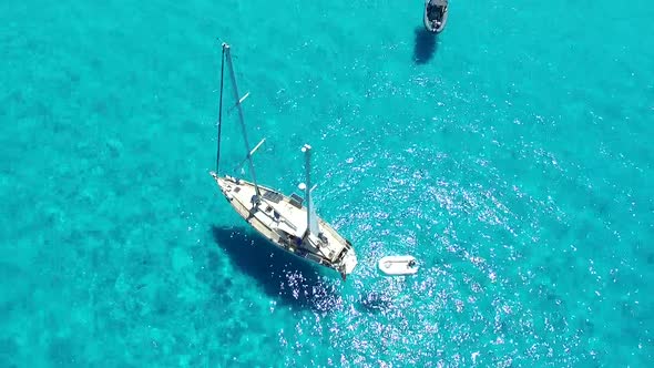 Sailing boat is floating on crystal clear blue water during summer sunny day. Areal shoot top above.