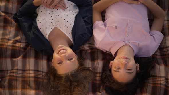 High Angle View of Two Smiling Teenage Cute Girls Looking at Camera Lying on Blanket in Park