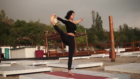 Woman Practicing Yoga on Mat on the Beach Performing Yoga Asanas or Stretching Legs Leaning Torso