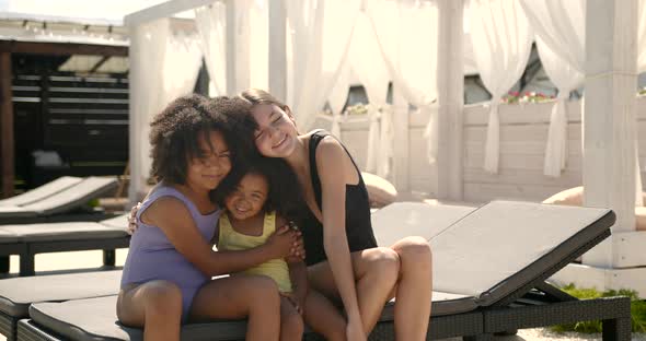 Mixed Race Little Girls Embracing on Lounger By Pool