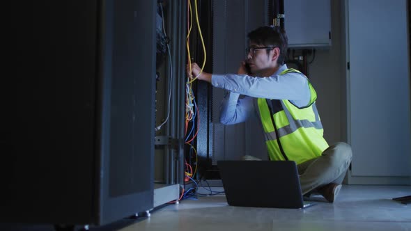 Asian male it technician using smartphone and laptop checking computer server