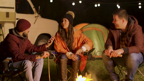 Group of Close Friend Relaxing Together Around Camp Fire in a Cold Night of Autumn