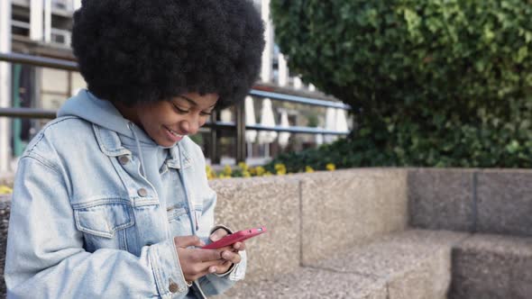 Young African American Woman Using Mobile Phone While Sitting Outdoors