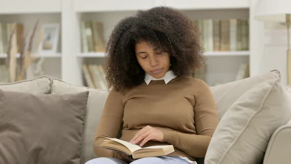 Young African Woman Sitting Reading Book on Sofa