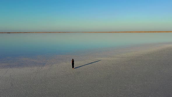 A beautiful top view of a woman in a black dress who walks on a salty, pink lake.