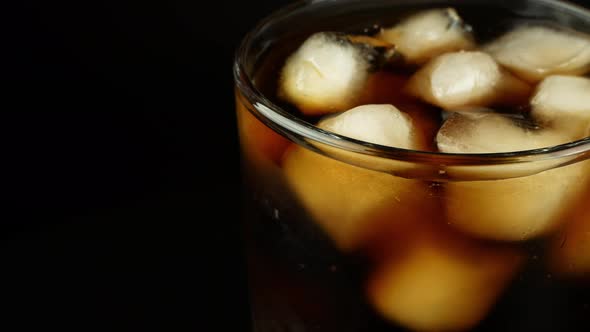 Rotation of a glass with ice cubes and a cola drink on a black background.