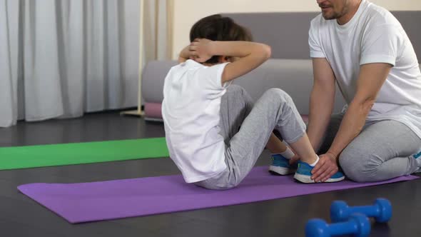 Boy Doing Sit-Ups at Home With Help of Father, Family Training, Sport Childhood