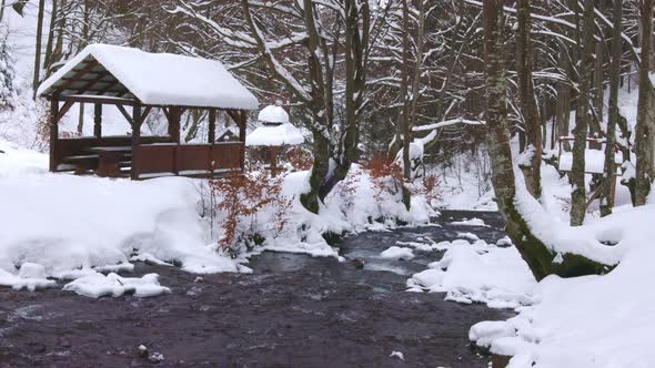 A Wooden Gazebo in the Depths of the Forest Near a Mountain Stream and People Walk Past It Climbing