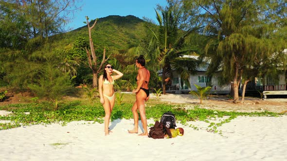 Beautiful smiling ladies on photoshoot having fun at the beach on summer white sand and blue 4K back