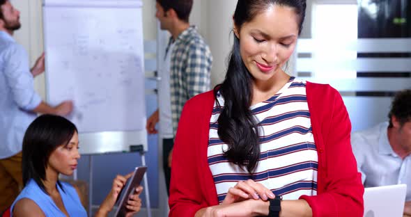 Female business executive adjusting time on smartwatch while coworker working in background