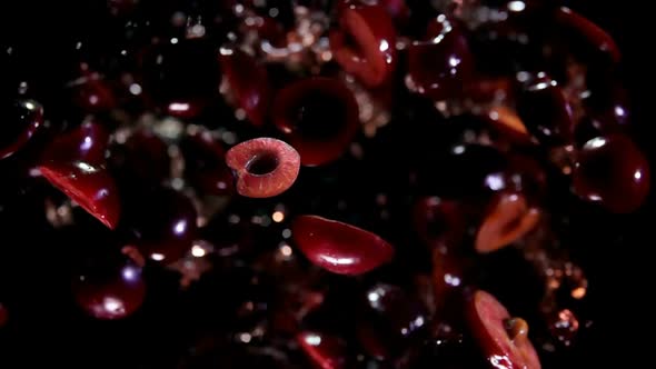 Halves of Cherries Are Bouncing Up with Splashes of Juice on a Black Background