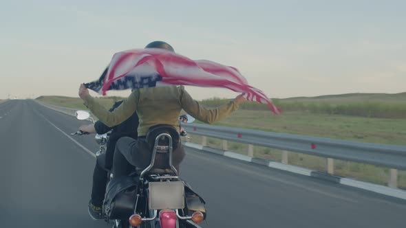 Couple is Riding Motorbike on Asphalt Highway Woman is Holding American Flag in Her Hands Which is