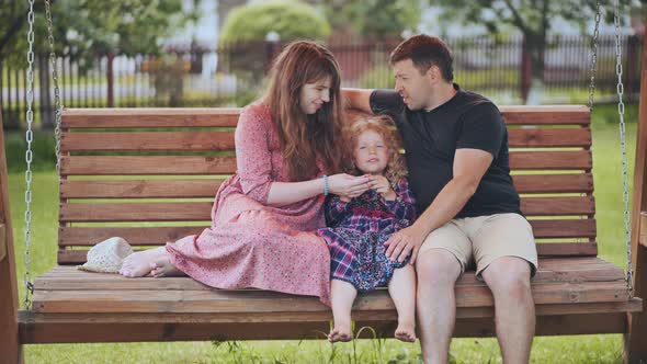 Portrait of a Young Family on a Swing in the Garden