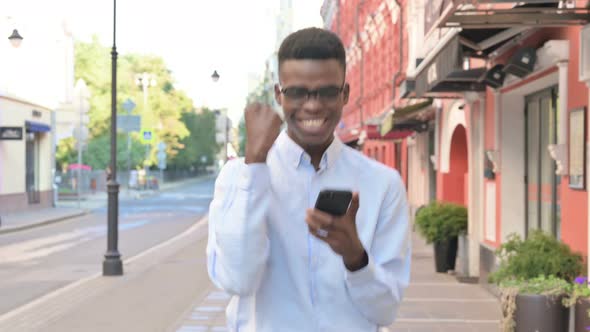 Walking African Man Having Success on Smartphone