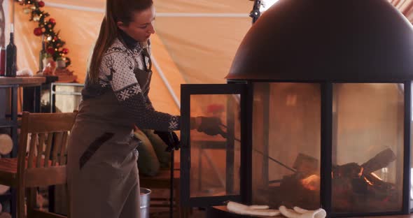 Caucasian Woman in Apron Move Wood in Fireplace with Fire Poker in Cosy Cafe Indooors for Heat