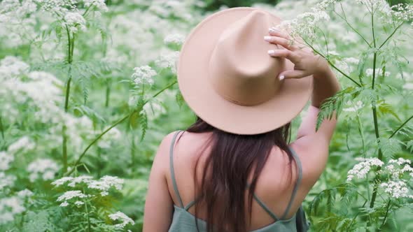 Young Beautiful Woman Posing in a Forest with a Hat on a Background of White Flowers. Happy Brunette