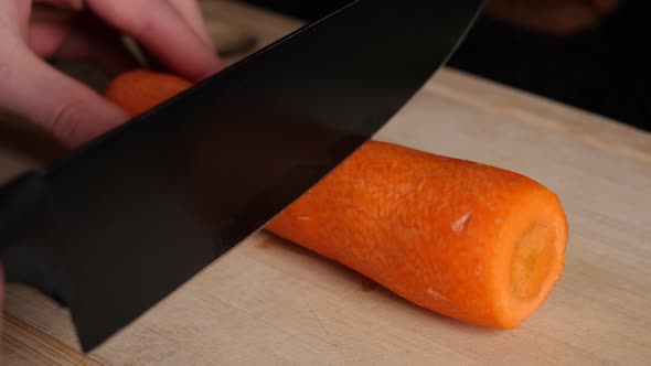 Black knife cuts three pieces out of a fresh carrot in slow motion.