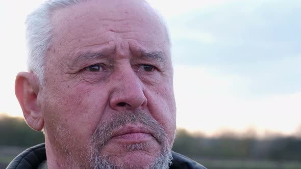 Closeup Portrait of a Bearded Gray Mature Man Pensively Sitting at Home in the Yard