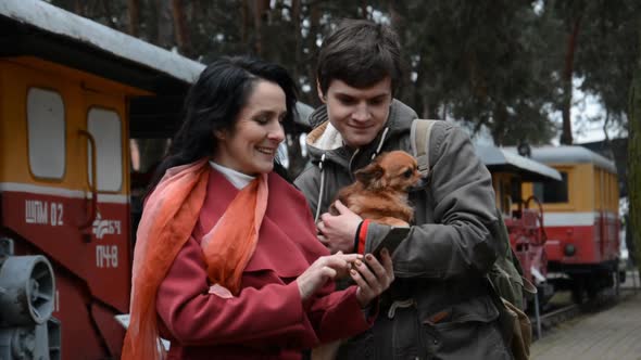 A Woman and a Young Guy with a Dog Are Watching Something on the Phone