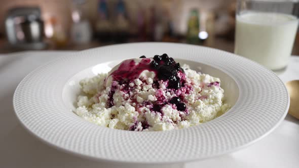 Fresh cottage cheese with sour cream and blueberry jam in white plate rotates