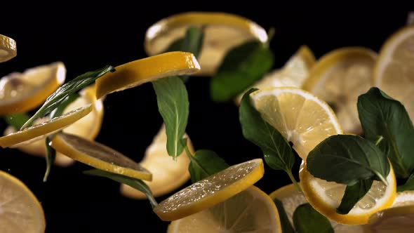 SUPER SLOW MOTION Shot of Fresh Sliced Lemon and Mint Leafs Flying Against Black Background