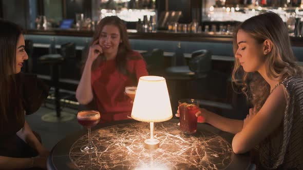 Three Happy Young Women Sitting at the Small Table in Bar