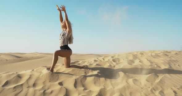 Woman is Throwing Sand on the Wind in the Desert While Kneeling on a Dune