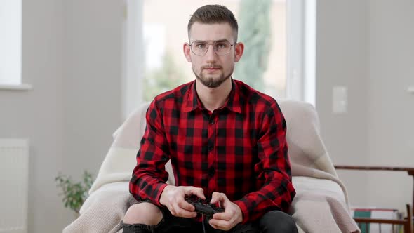 Unhappy Young Man in Eyeglasses Losing in Video Game Leaning Back on Armchair
