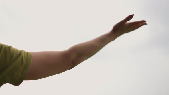 Hand of Young Woman Under Warm Rain Drops Against Grey Sky