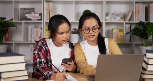 Twin asian girls using laptop and smartphone to learning online