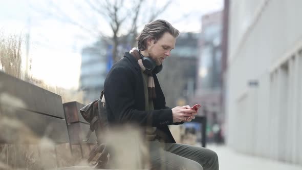 stylish guy in scarf and coat hold mobile phone in a hand at street of Wroclaw, Poland