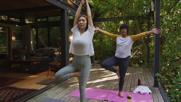 Asian mother and daughter practicing yoga outdoors in garden