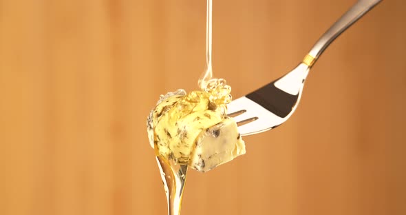 Liquid Organic Honey Dripping on a Fork with Dorbly Cheese on a Light Background. Healthy Food