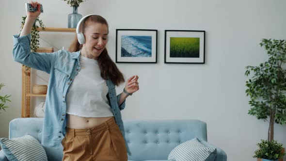 Playful Woman Student Singing in Remote Control and Dancing Listening to Music in Headphones at Home
